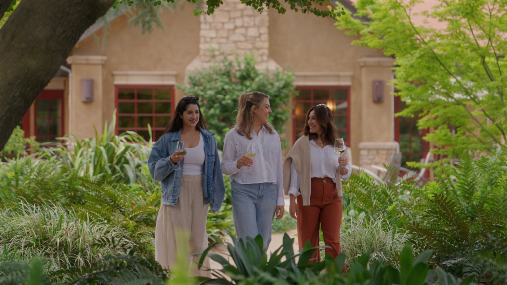 Three women with wine glasses walking through the garden at Harney Lane winery in Lodi.