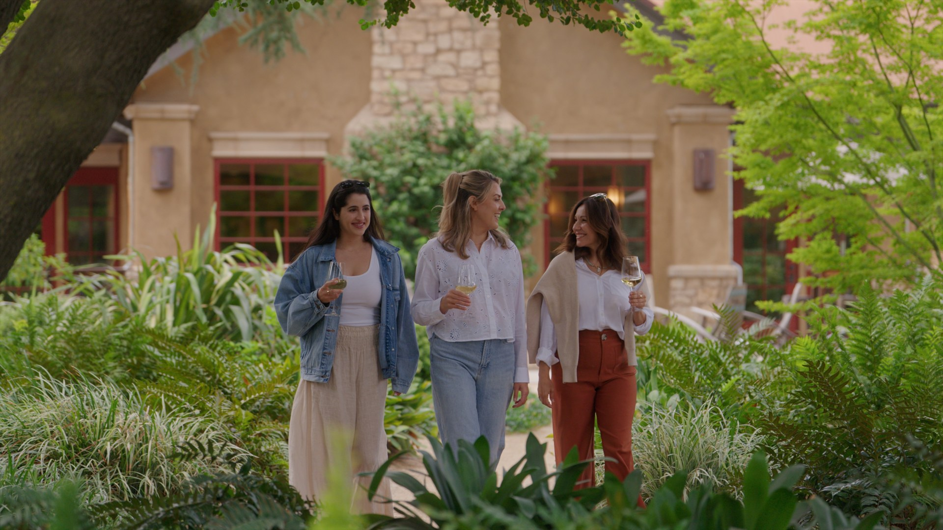 Three women walking through the Harney Lane garden with wine glasses